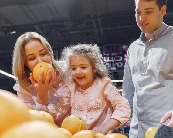 Family enjoying a cheerful shopping trip together at the grocery store, selecting fresh oranges.